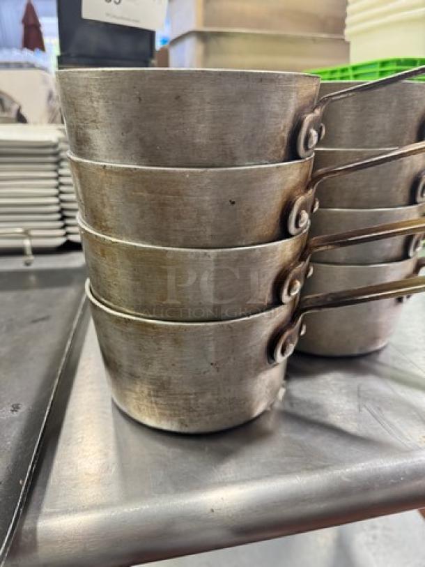 Stack of 6" saucepans, model BIDX8, stainless steel, used condition, with riveted handles, shown on a metal surface.