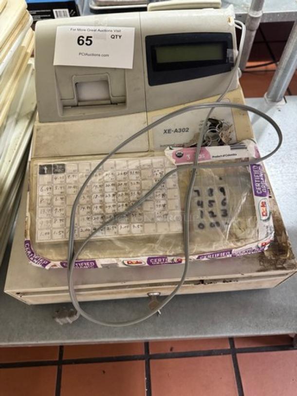 Sharp XE-A302 cash register with worn keyboard, display screen, and attached cable. Shows signs of heavy use.