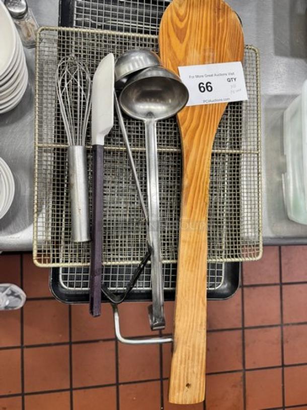 Assorted kitchenware including a large wooden spoon, ladle, knife, and whisk on a metal rack with auction tag labeled "66".