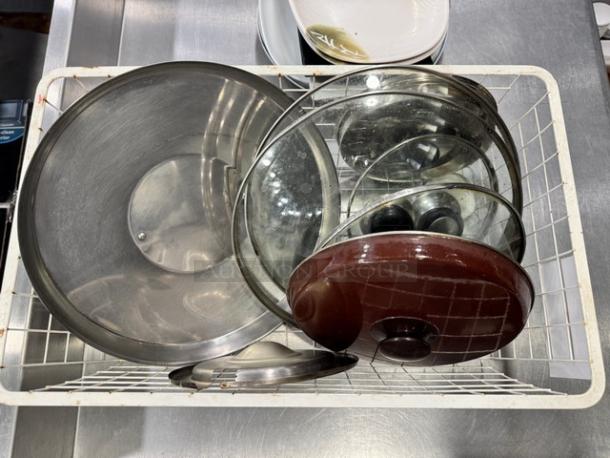 Assorted glass and aluminum pot lids in a metal basket, includes round glass with knobs and metal lids, various sizes, used condition.