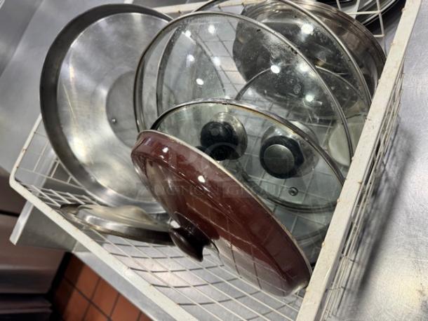 Miscellaneous glass and aluminum pot lids in a wire basket, various sizes and conditions, featuring knobs and metal rims.