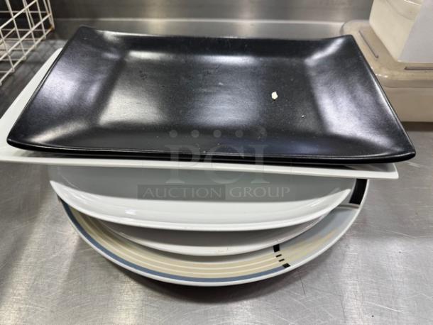 Assorted serving platters, various shapes and sizes, stacked. Includes black and white rectangular, and round platter with stripe.