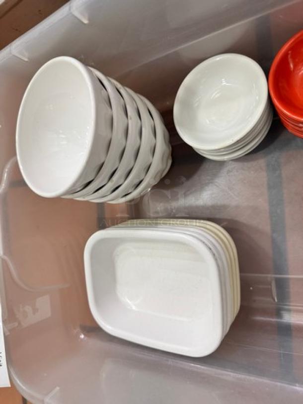 Mixed kitchenware lot containing stacked white bowls and rectangular dishes in a plastic bin. No visible markings.