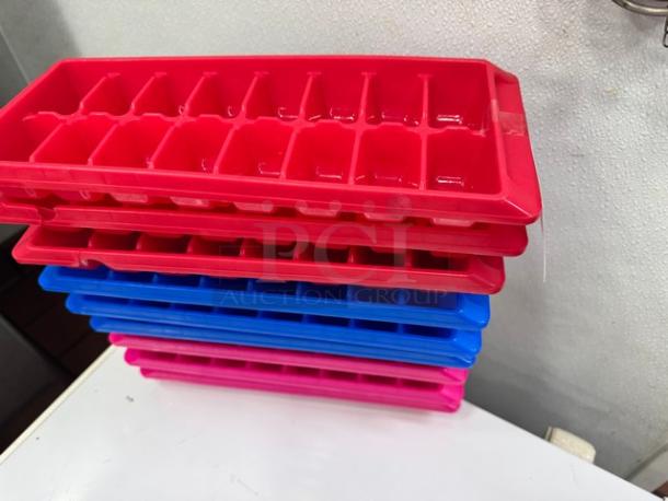 Lot of 9 ice cube trays, red, blue, pink, in good condition. Stacked on a white surface. No visible markings.
