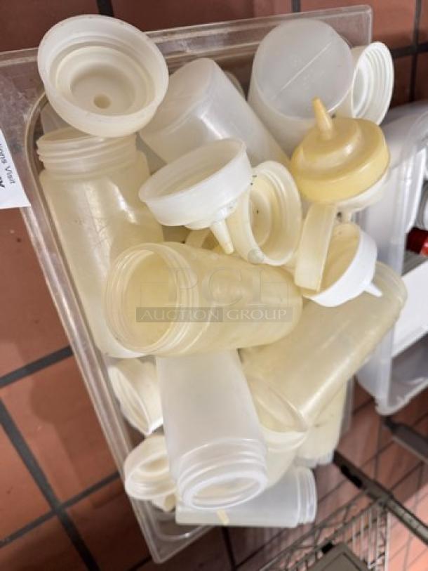 A collection of used plastic squeeze bottles, assorted sizes, in a clear container. Some bottles have attached caps.