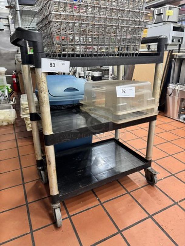 Three-tier metal and plastic bus cart with wheels. Shows wear and some discoloration. Includes tags labeled "82" and "83".