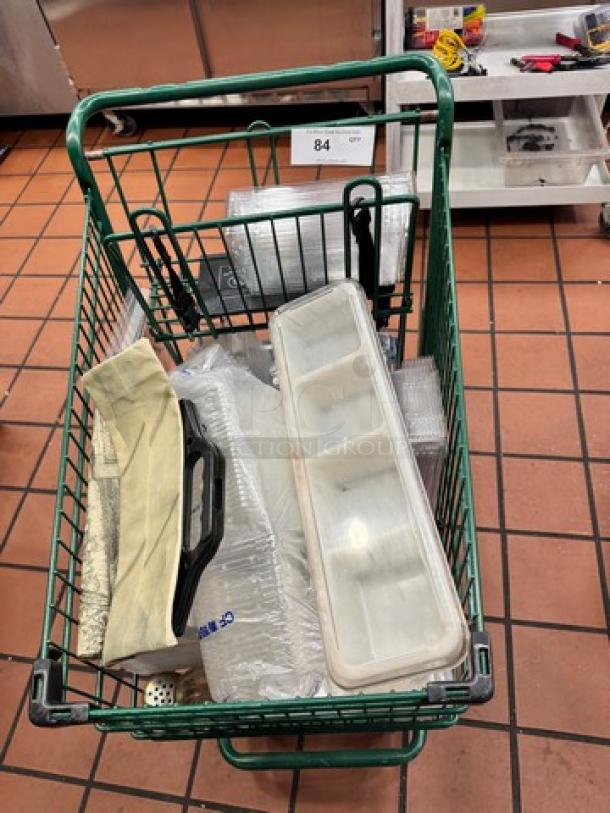 Green metal shopping cart containing assorted kitchen items, including trays and tools. Auction tag 84 visible.