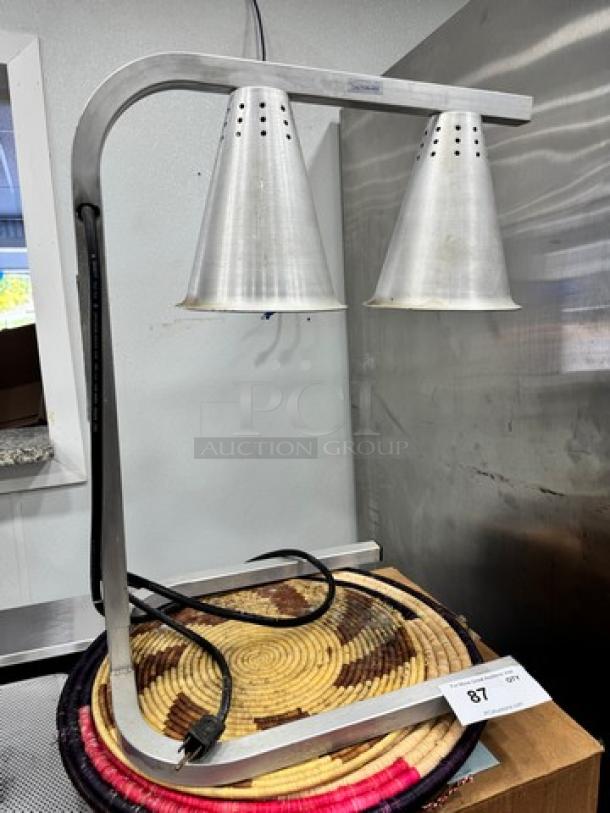 Commercial food heat lamp with dual metal shades, adjustable arm, and power cord. In good condition. Lot tag number 87 visible.