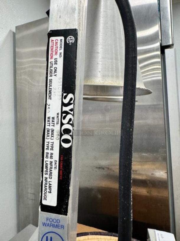 Sysco commercial food heat lamp with adjustable arm, in working condition. Label indicates model and safety instructions.