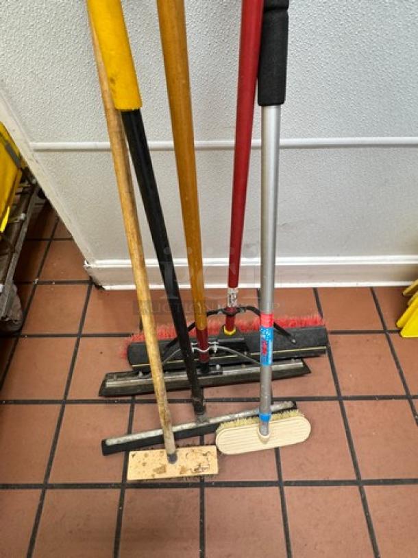 Assorted cleaning tools including mops and brooms with wooden and metal handles, some with visible wear.