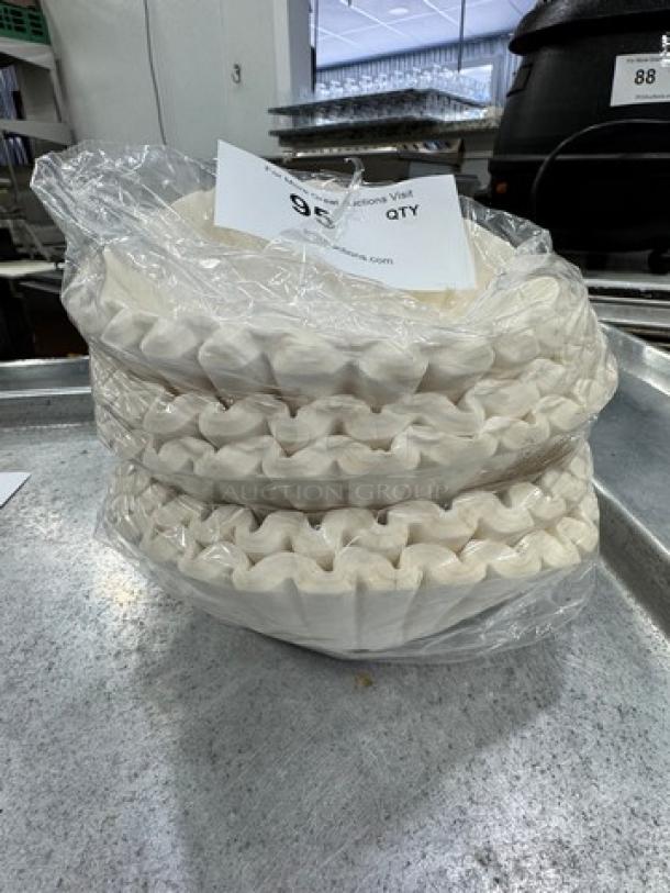 Stack of white paper coffee filters wrapped in clear plastic, new condition, on metal surface.