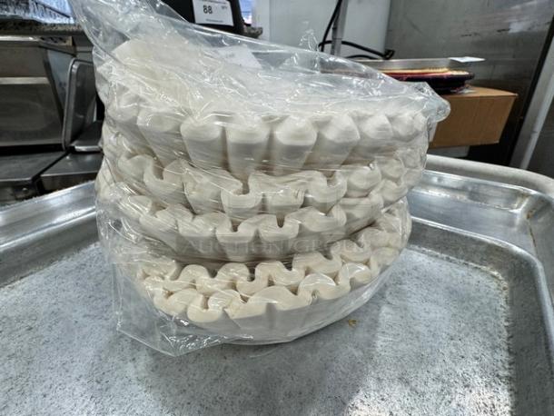 Stack of paper coffee filters in plastic packaging, pristine condition, on metal tray.