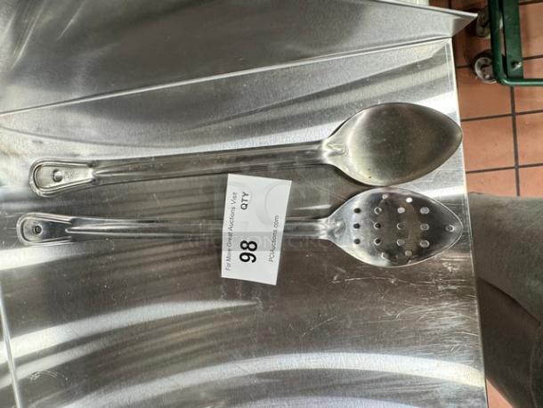 Two stainless steel kitchen spoons, one solid and one slotted, in good condition. Auction tag with "98 QTY" visible.