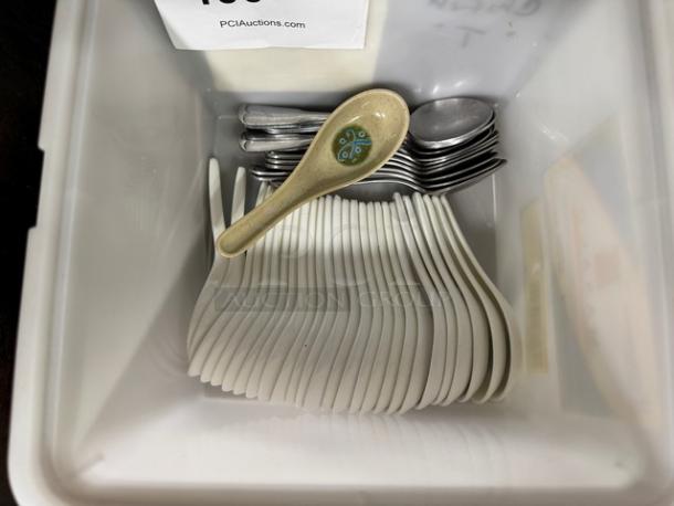 Assorted spoons in a bin, including decorative ceramic and metal spoons, all in used condition.