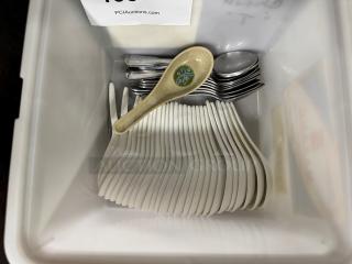 Assorted spoons in a bin, including decorative ceramic and metal spoons, all in used condition.