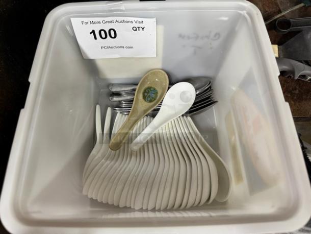Lot of miscellaneous spoons in plastic bin, includes white plastic and metal spoons. Tag indicates quantity of 100.