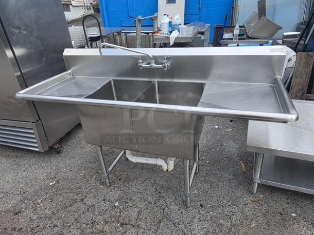 Stainless steel two compartment sink in good condition, integrated backsplash, and commercial faucet.