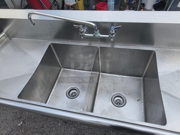 Stainless steel two-compartment sink with integrated faucet, showing minimal wear, ideal for commercial use.