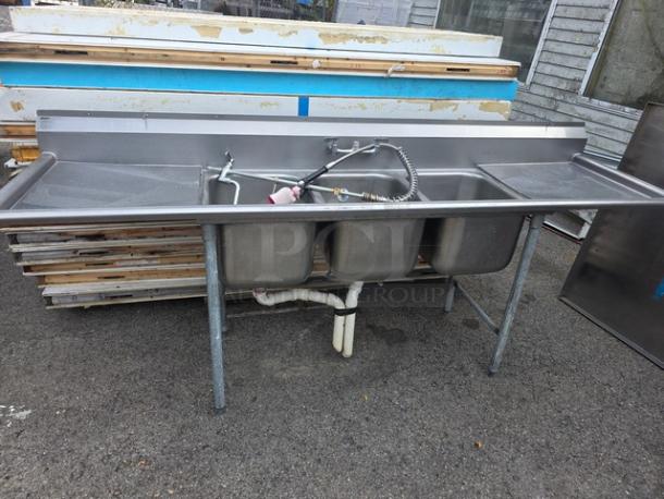 Stainless steel 3 compartment sink, commercial-grade, includes faucets and spray nozzle, used condition, slight surface wear.