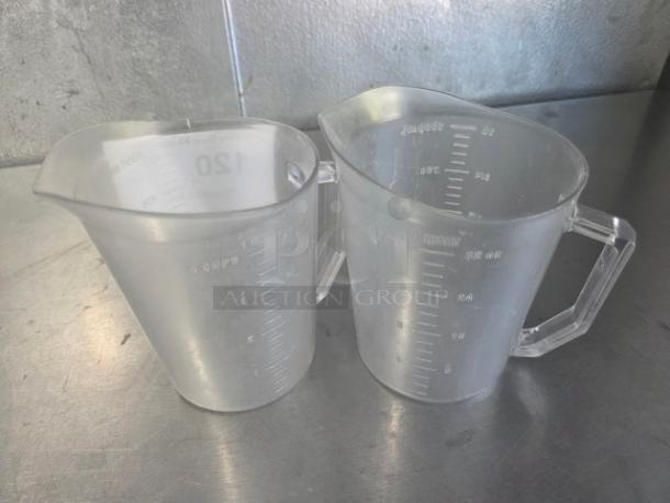 Two clear plastic measuring cups with engraved measurement markings on a metallic surface.