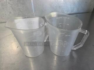 Two clear plastic measuring cups with engraved measurement markings on a metallic surface.