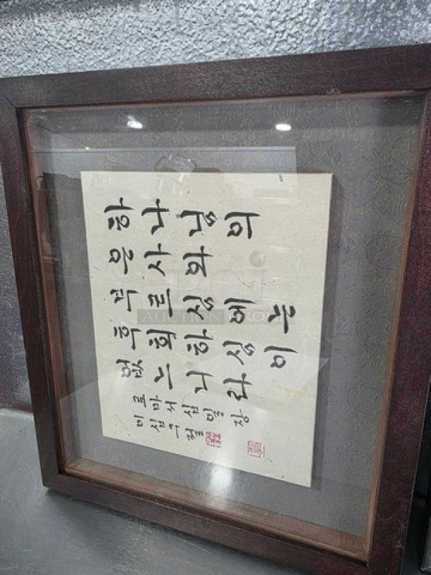 Framed artwork with calligraphy on textured paper, encased in a dark wood frame with glass. Signature markings in red.
