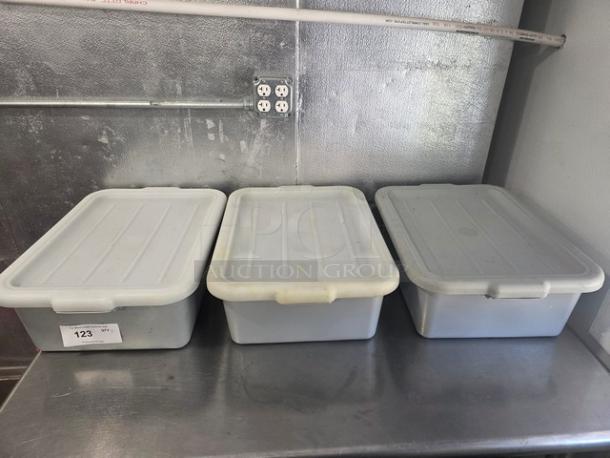 Lot of 3 plastic bus tubs with lids, gray color, good condition, placed on a metal counter. Marked 123 on the side.