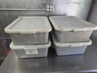 Lot of 4 plastic bus tubs with lids, used condition. Marked with "124 QTY." Stacked in pairs on a metal surface.