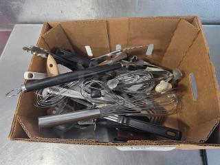 Lot of miscellaneous kitchenware in a cardboard box, including whisks, ladles, and tongs. Mixed materials, varied condition.
