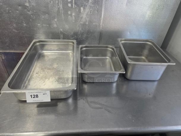 Lot of 3 stainless steel food pans in varying sizes, used condition, with auction tag "128" visible.