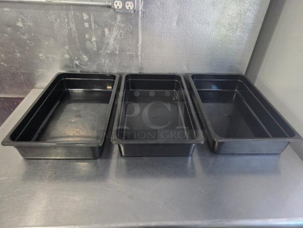 Lot of 3 black Cambro plastic food pans on metal surface. In good condition, ideal for food storage or service.