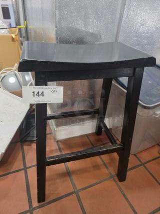 Black wooden bar stool, curved seat, sturdy frame. Slight wear visible. Auction label reads "144 QTY". Modern style.