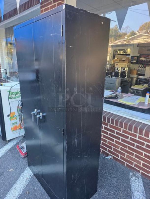 Black metal storage cabinet, two doors with handles, showing visible wear and scratches.
