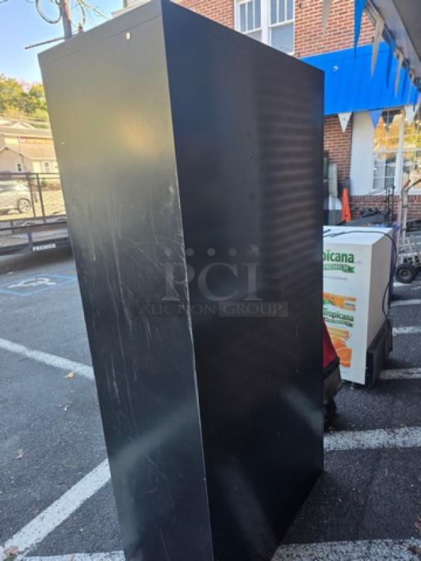 Black metal storage cabinet, tall and rectangular, with visible scratches. Ideal for garage or office organization.