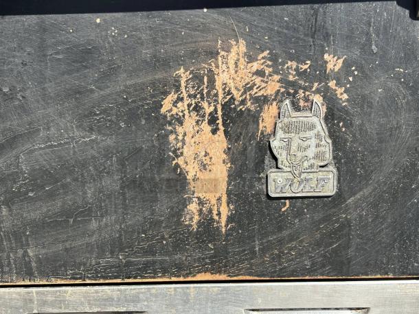 "WOLF" logo on commercial 6-burner range and oven front panel with visible wear, in excellent working condition.