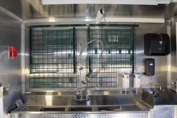 NEW 24' Cruising Kitchens food trailer interior with stainless steel fixtures, sink, dish racks, and soap dispensers.