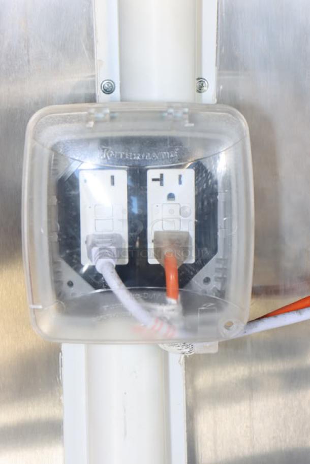 Electrical outlet with cords inside a clear protective cover against a stainless steel surface in a new Cruising Kitchens food trailer.