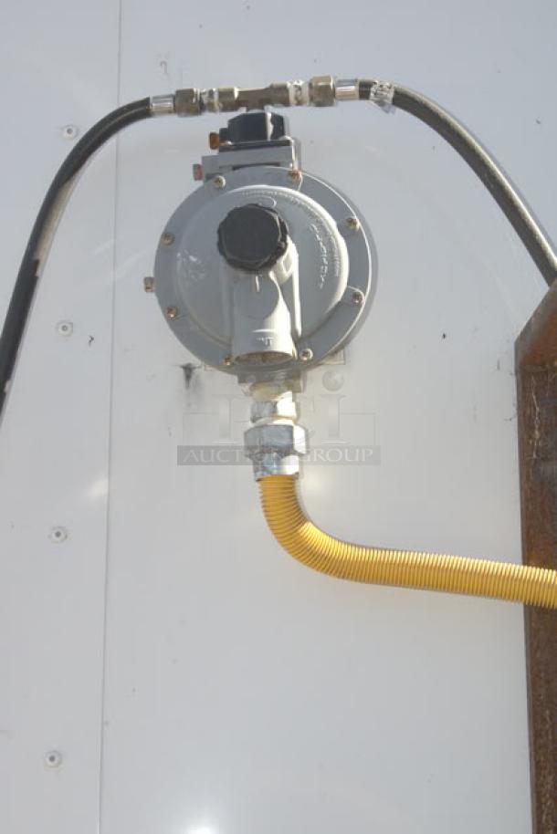 Gas hookup on Cruising Kitchens 24' Enterprise Food Trailer, featuring a silver regulator and yellow propane hose.