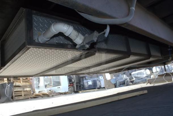 The undercarriage of a new Cruising Kitchens 24' food trailer with visible plumbing and diamond plate panels.