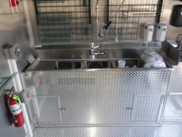 Inside view of the 2023 Cruising Kitchens food trailer with stainless steel sink, faucet, and storage. Features diamond plate finish.