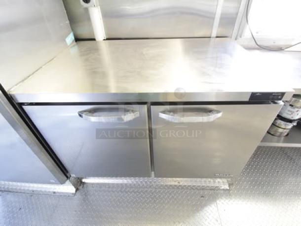 Brand new 2023 Cruising Kitchens 24 ft. Enterprise food trailer interior. Stainless steel counter and double-door cooler visible.