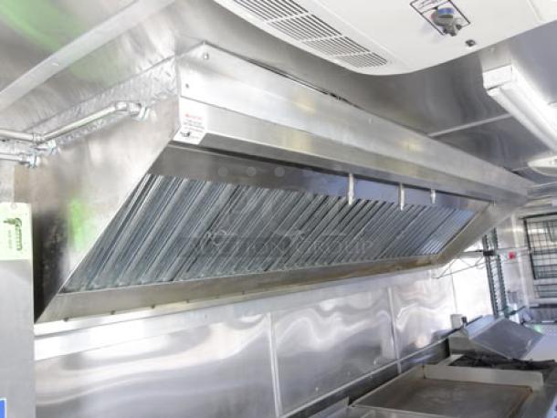 Brand new 2023 Cruising Kitchens food trailer interior showing 12ft hood with ANSUL system, stainless steel finish, appliances.