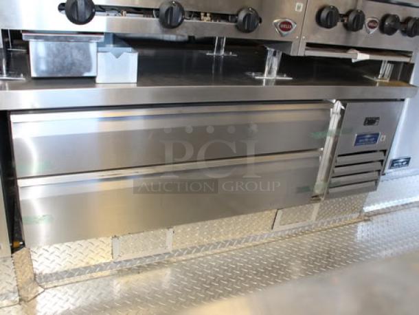 Alt text: Stainless steel commercial-grade kitchen appliances inside a 2023 Cruising Kitchens 24 ft. food trailer. Features include coolers, deep fryers, and a range.