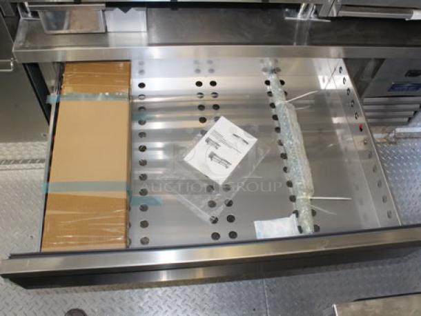 Brand new 2023 Cruising Kitchens 24 Ft. Enterprise Food Trailer drawer with packaging, instruction manual, and stainless steel interior.