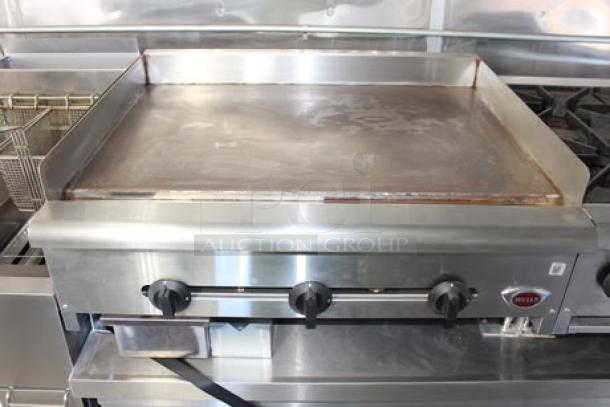 Commercial-grade griddle in a 2023 Cruising Kitchens Enterprise food trailer, featuring three control knobs and stainless steel construction.