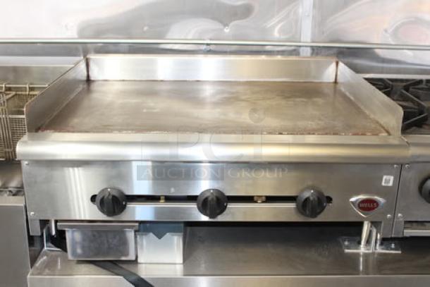 Griddle inside the 2023 Cruising Kitchens 24 Ft. Enterprise Food Trailer. Stainless steel, commercial-grade, with three control knobs.