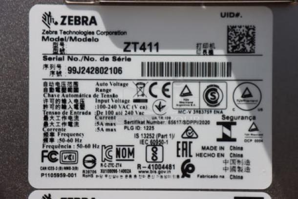 Zebra ZT411 industrial barcode printer label with model ZT41142-T410000Z, S/N 99J242802106, voltage and compliance details.