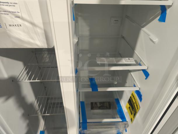Brand new Frigidaire side-by-side refrigerator, model FRSS2323AW, 22.3 cu ft. Interior shows shelves with protective tape.