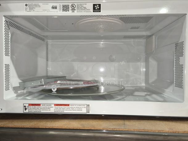 NEW GE 1.6 cu ft over-the-range microwave oven, model JVM3160DF9WW. Interior view with glass turntable and installation manual.