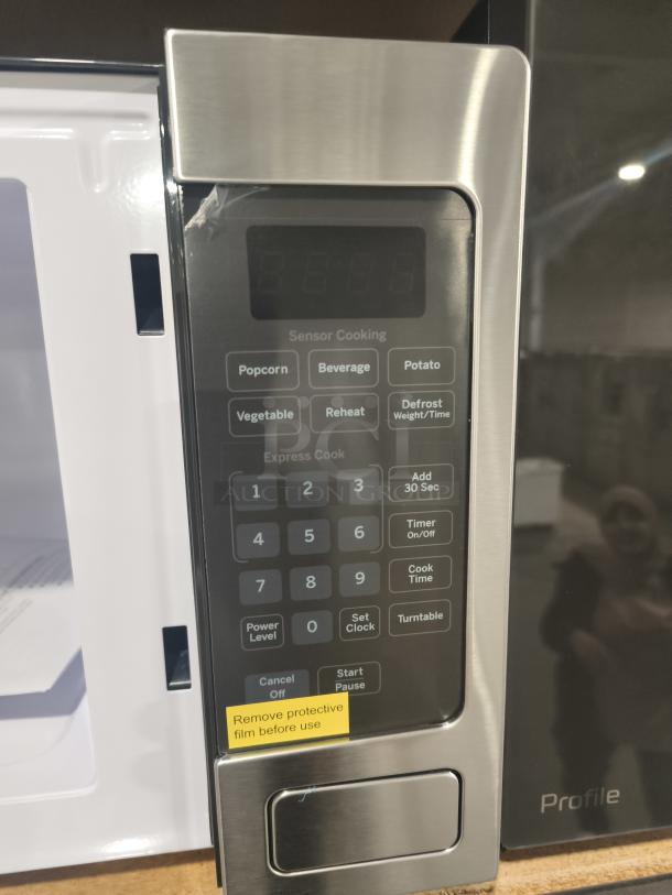 GE Profile PEM31SFSS microwave, 1.1 cu ft, stainless steel, brand new scratch and dent condition. Control panel features sensor cooking and express cook options. Yellow sticker notes, "Remove protective film before use."